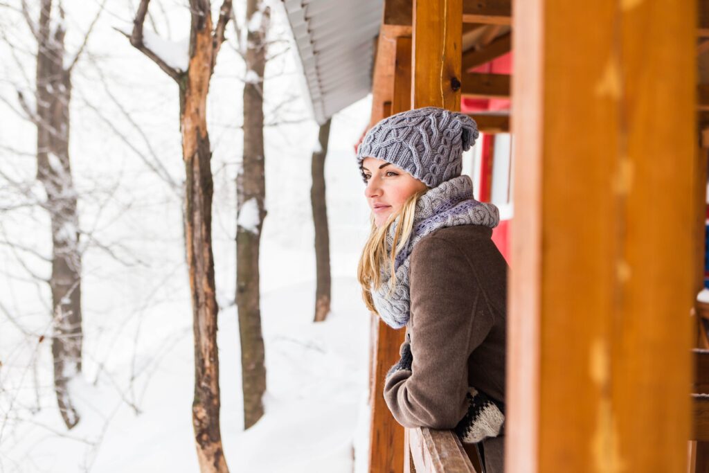 Young woman dressed warmly in a cozy knit hat and scarf, enjoying a winter day outdoors in a snowy forest setting.